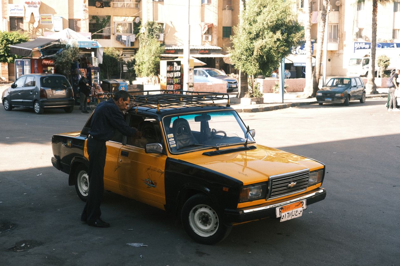 A classic yellow taxi cab at a bustling street scene in Alexandria, Egypt, with vivid urban life.